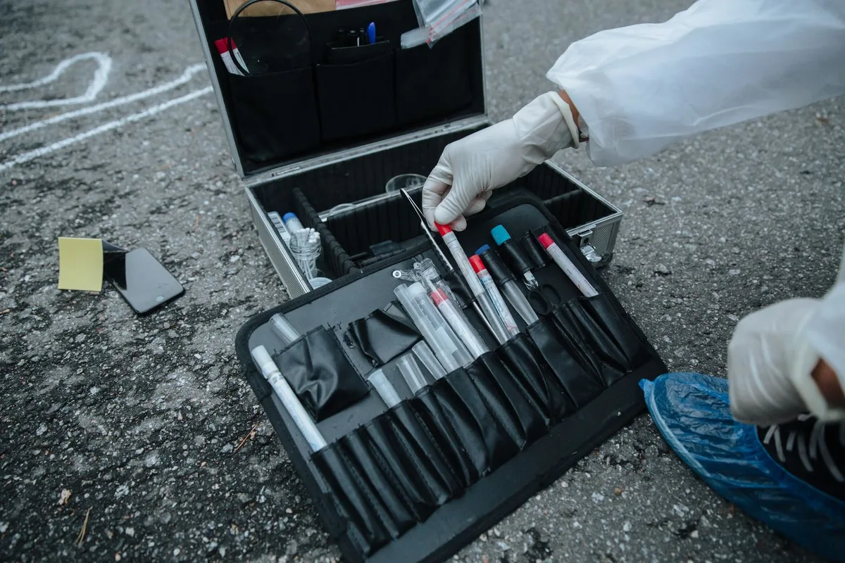Maleta de coleta forense aberta no chão, com tubos e mãos enluvadas